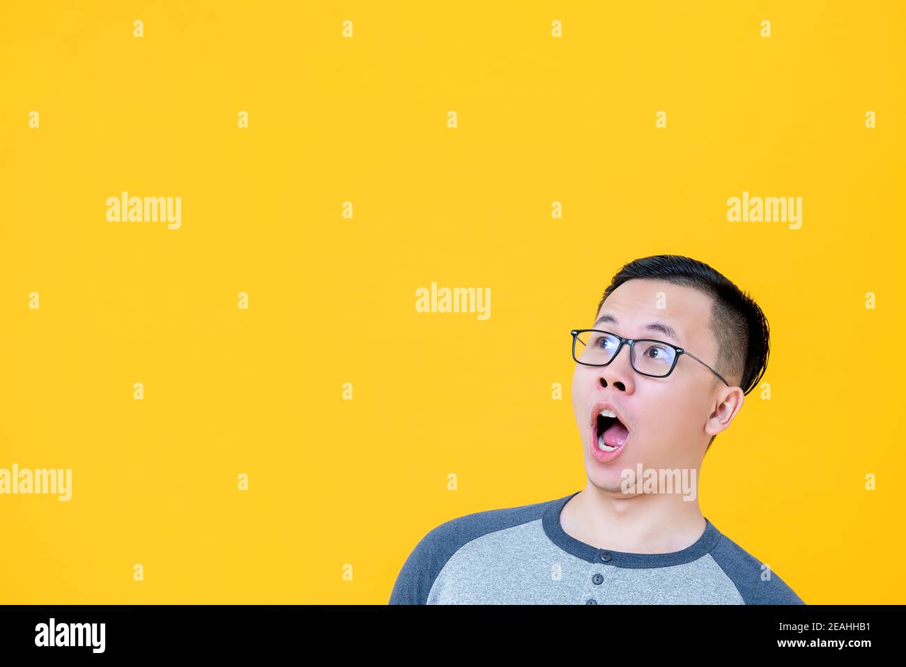 Shocked Asian man gasping and looking to copy space aside on yellow background Stock Photo