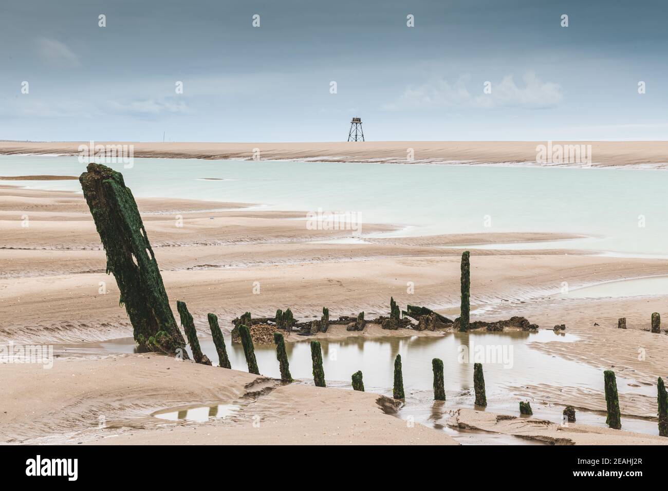 Epave de bateau avec en arrière plan le Phare de Walde.Le phare de Walde, France, Pas de Calais. C'est un phare dont l'architecture est unique en Fran Stock Photo