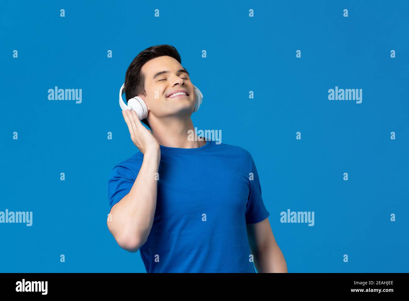 Relaxing young man listening to music from headphones with eyes closed isolated on blue background Stock Photo