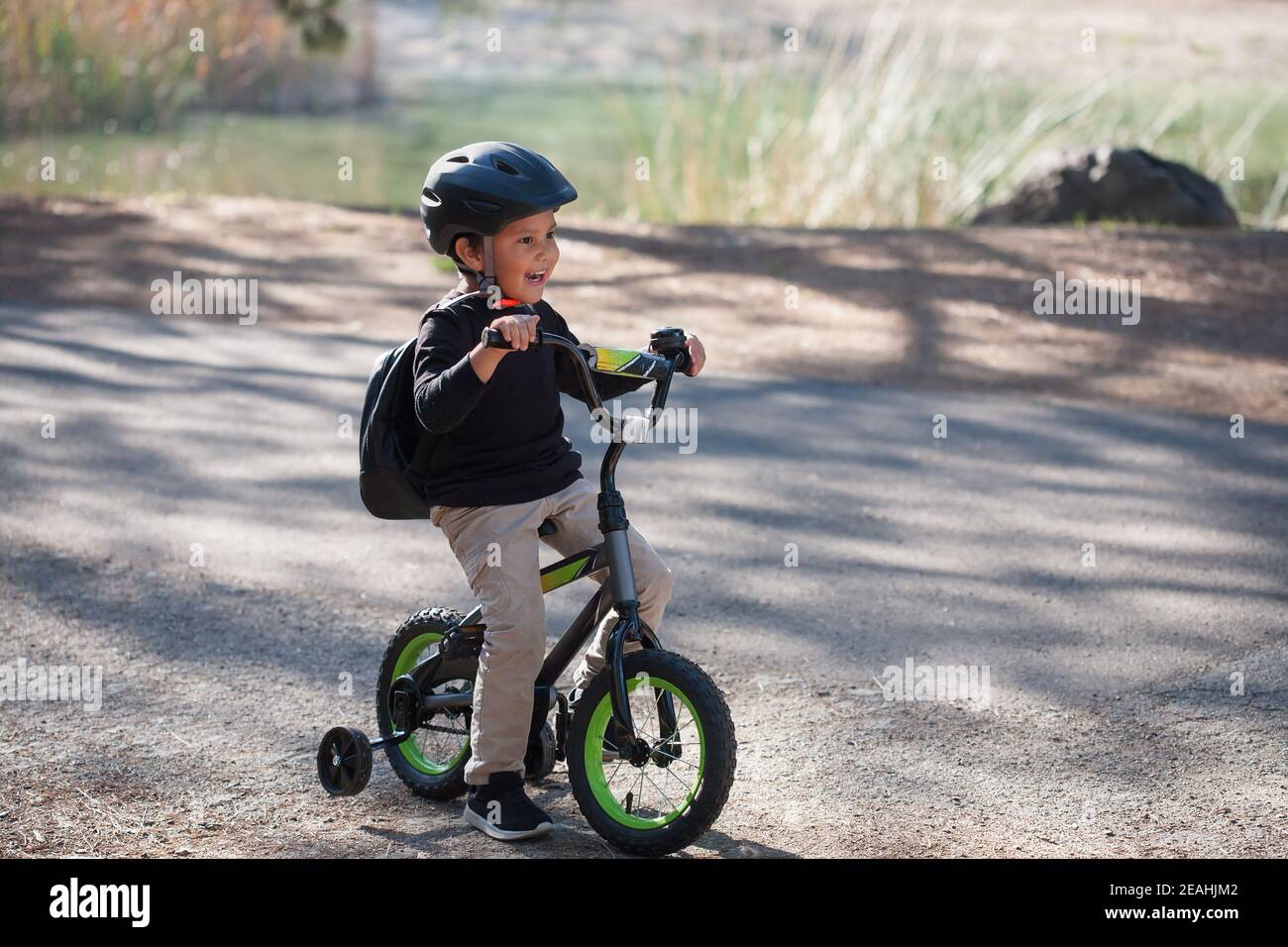 A five year old boy learning to ride a bicycle with training wheels, and a lake in the background. Stock Photo