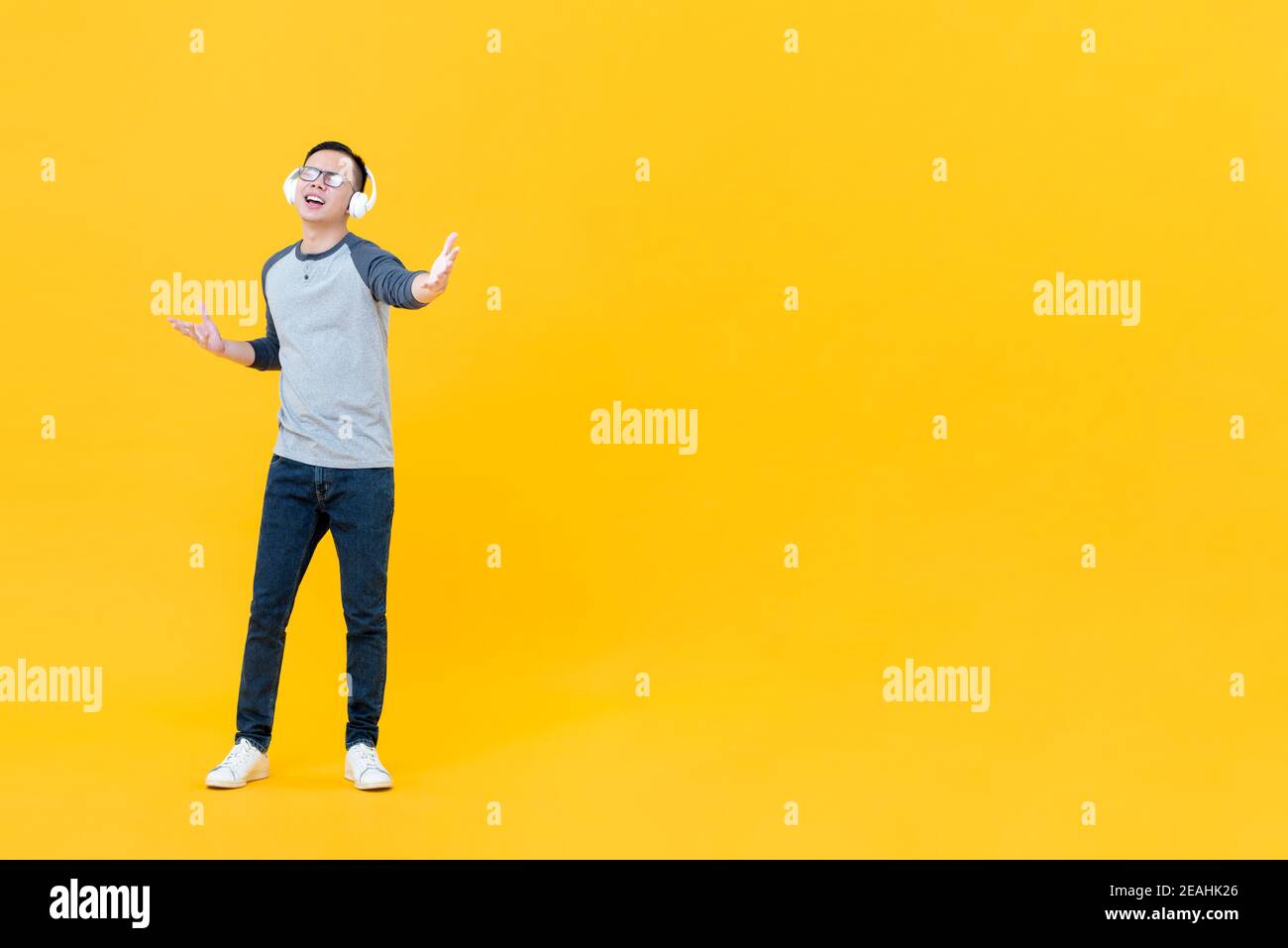Happy Asian man enjoyed listening to music on headphones with eye closed and hands open isolated on yellow background with copy space Stock Photo