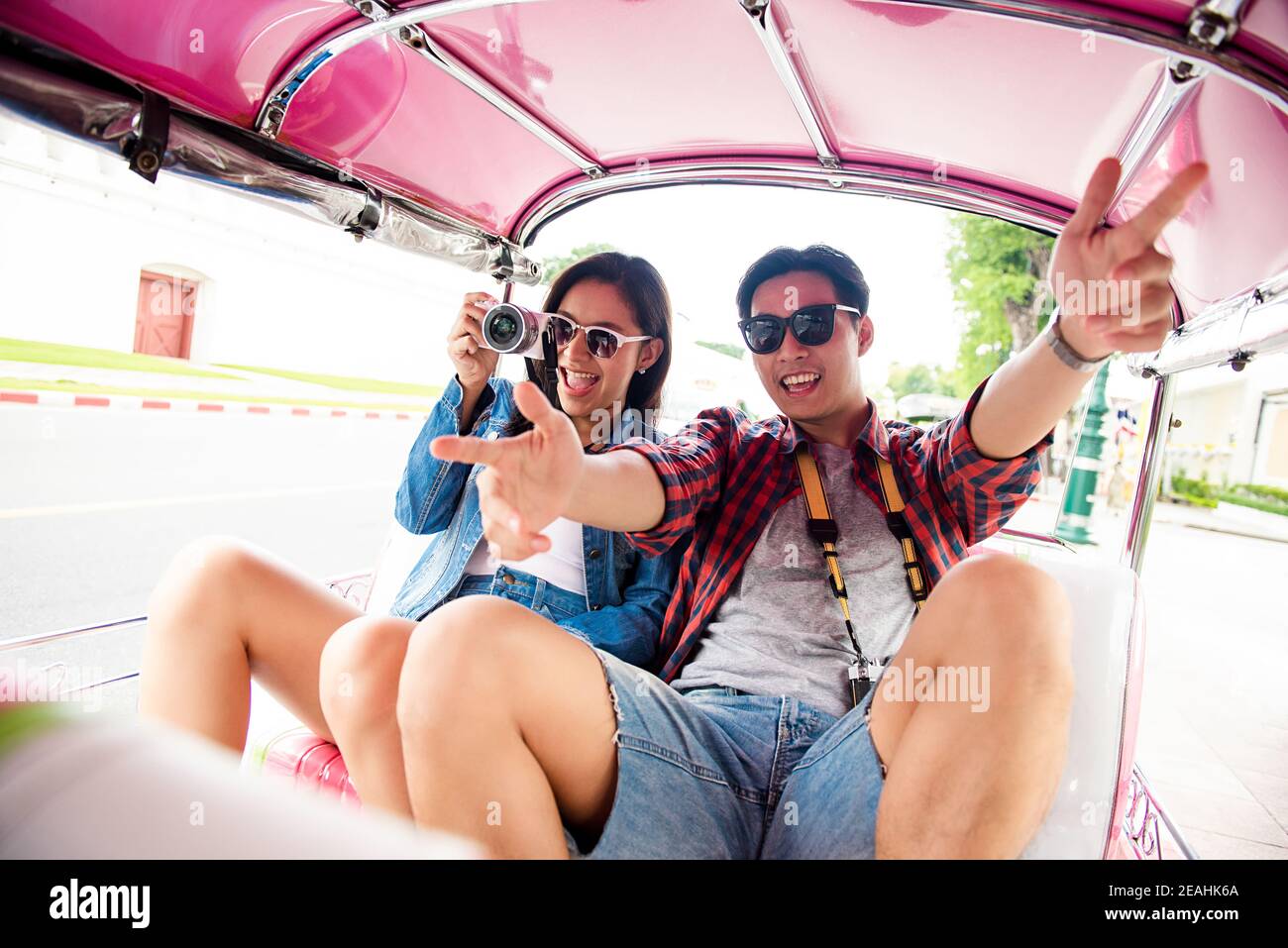 Young Asian tourist couple taking pictures and feeling excited while traveling on local Tuk Tuk taxi in Bangkok city Thailand Stock Photo