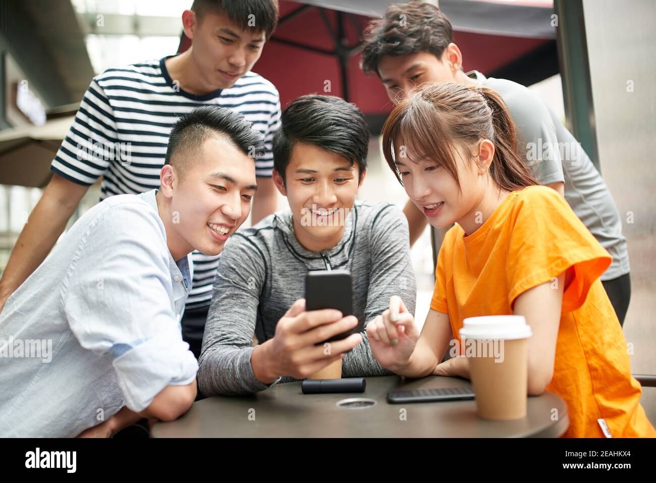 group of young asian adults four men and and a woman looking at mobile phone together outdoors Stock Photo