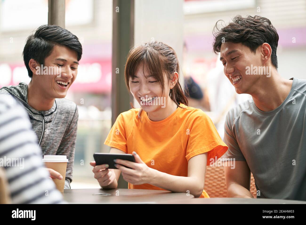 three young asian adults sitting in outdoor coffee shop using cellphone together Stock Photo