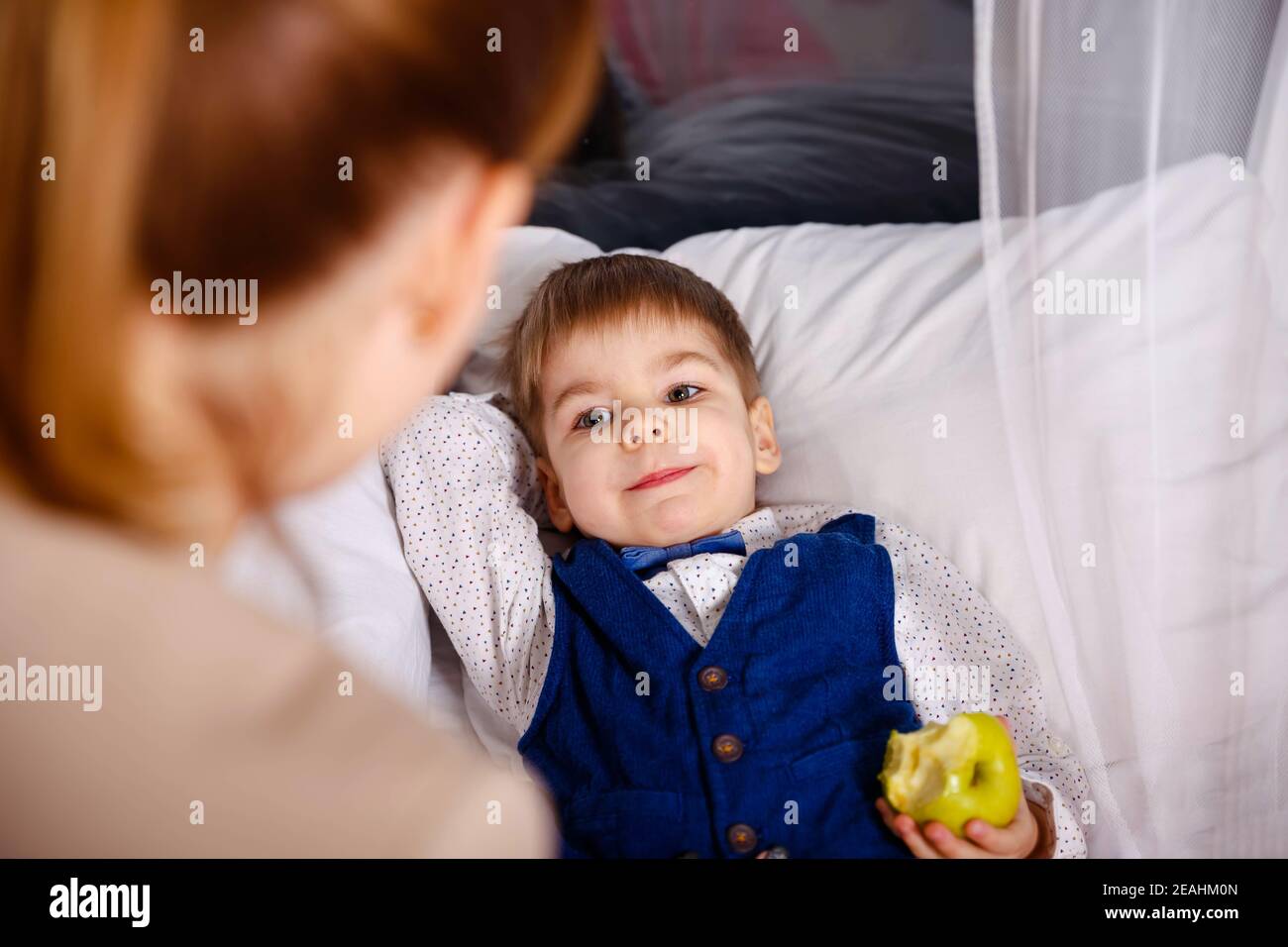 Mother giving good night kiss to sleeping son. Mom putting son to bed