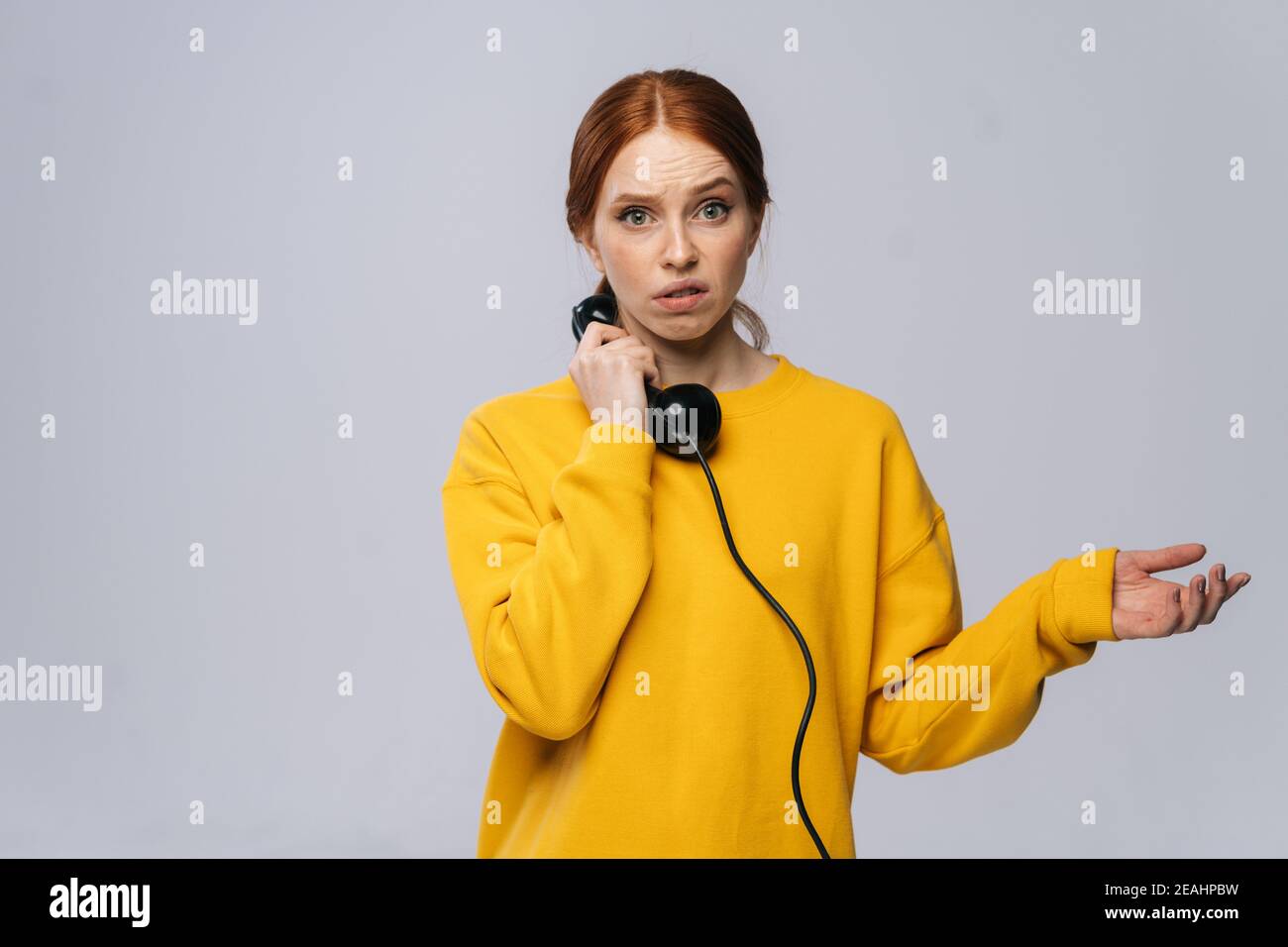 Disappointed sad young woman in stylish yellow sweater talking on retro phone and looking at camera Stock Photo