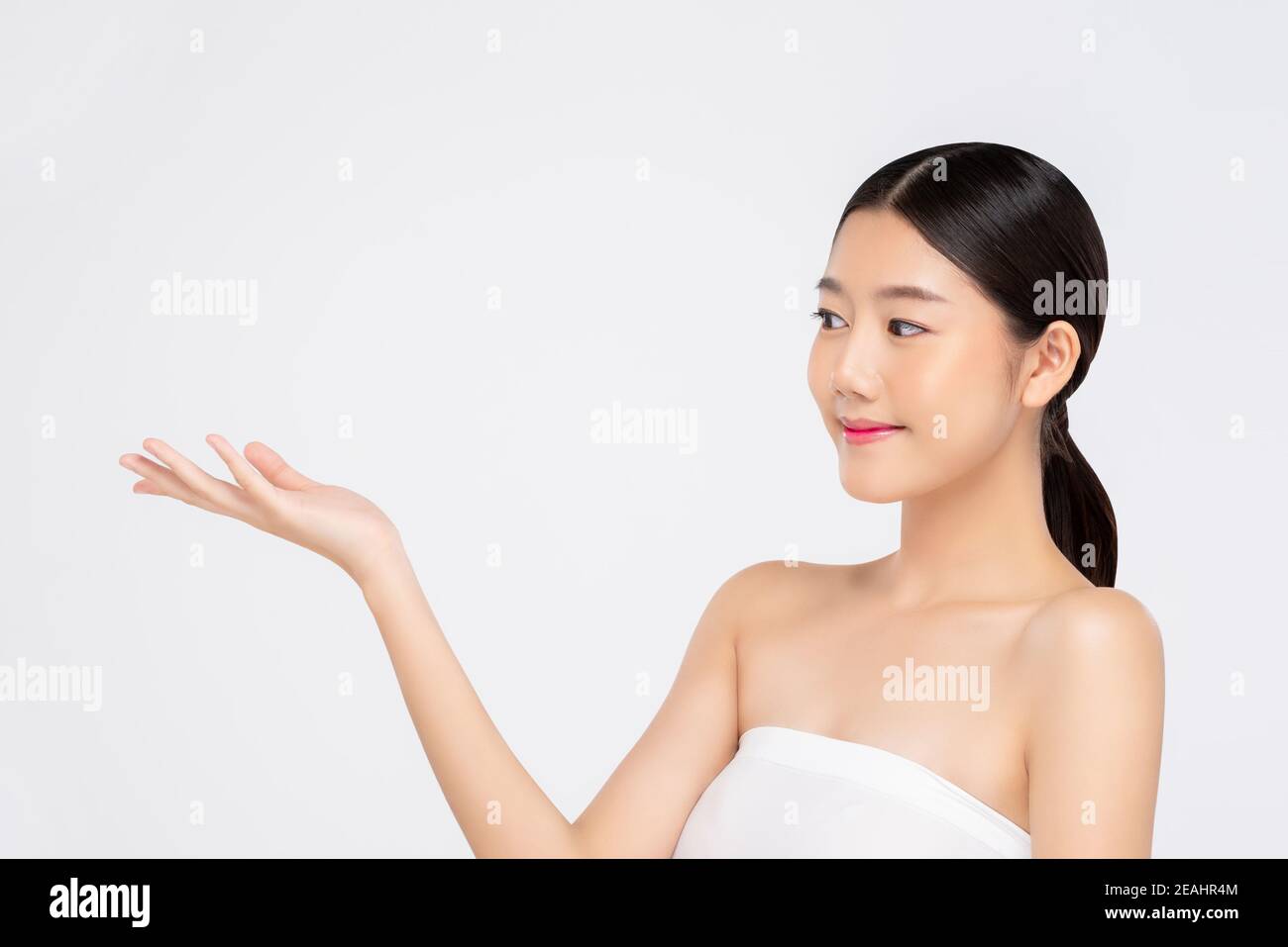 Young beautiful Asian woman with fresh clean appearance smiling and looking sideways at empty open hand isolated on white background for beauty and sk Stock Photo