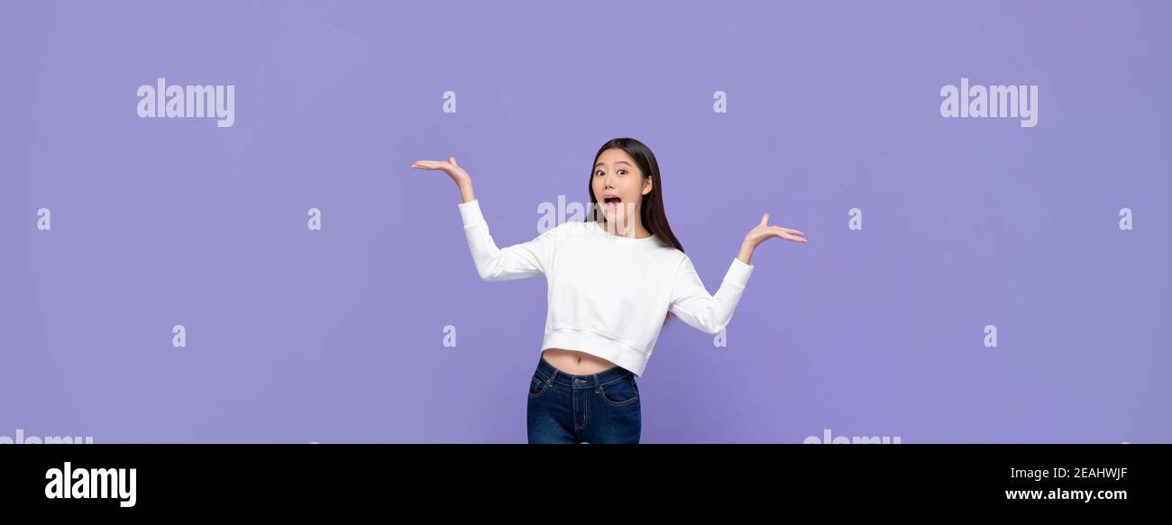 Beautiful excited young Asian woman doing presenting gesture with both hands open isolated on purple banner background Stock Photo