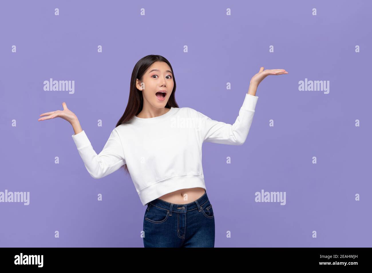 Beautiful excited young Asian woman doing presenting gesture with both hands open isolated on purple background Stock Photo