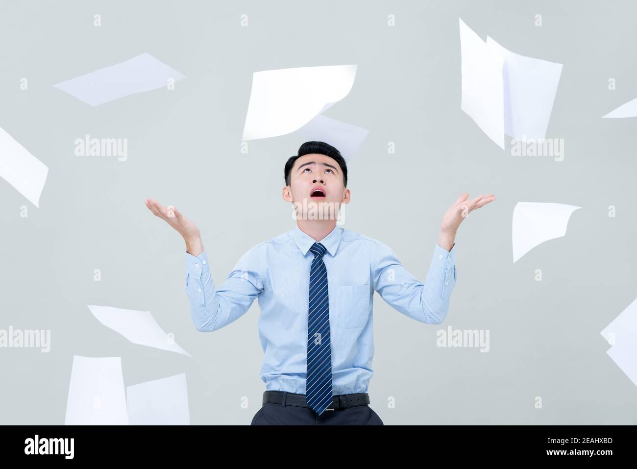 Busy Asian business man overwhelmed by too much work and surrounded by flying paper Stock Photo