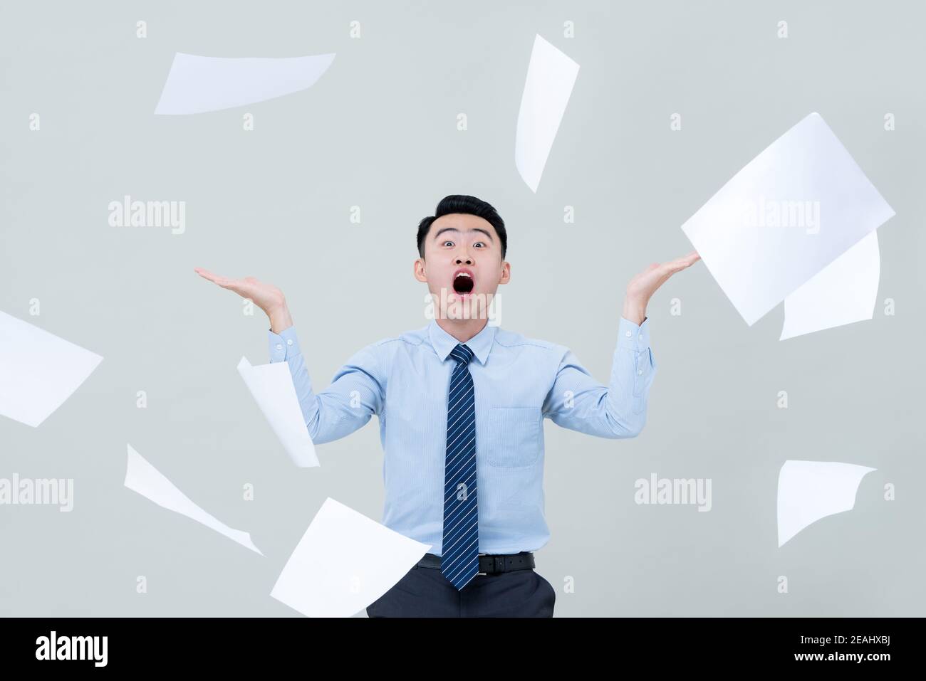 Busy funny Asian business man overwhelmed by too much work and surrounded by flying paper Stock Photo