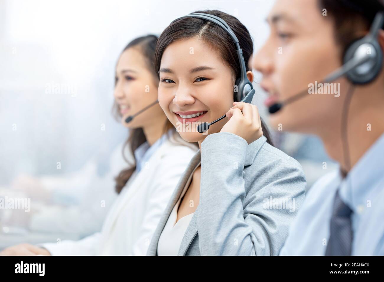 Smiling beautiful Asian woman telemarketing agent working in call center office with team Stock Photo