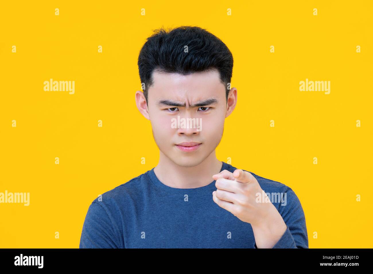Close up portrait of serious young cute Asian boy pointing finger at you isolated on yellow background Stock Photo