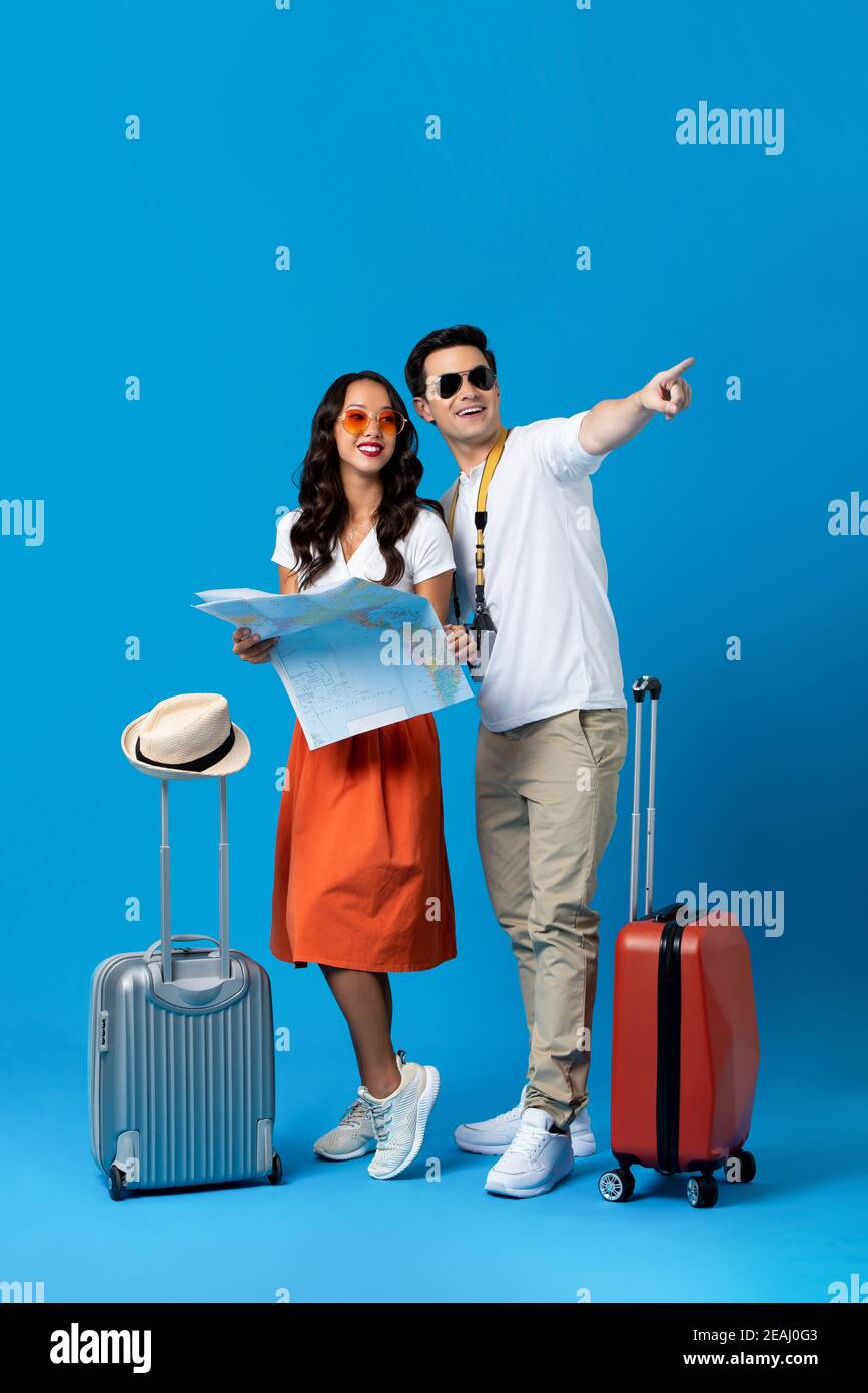 Happy smiling interracial tourist couple with baggage enjoying their summer vacation getaway together in blue studio background Stock Photo