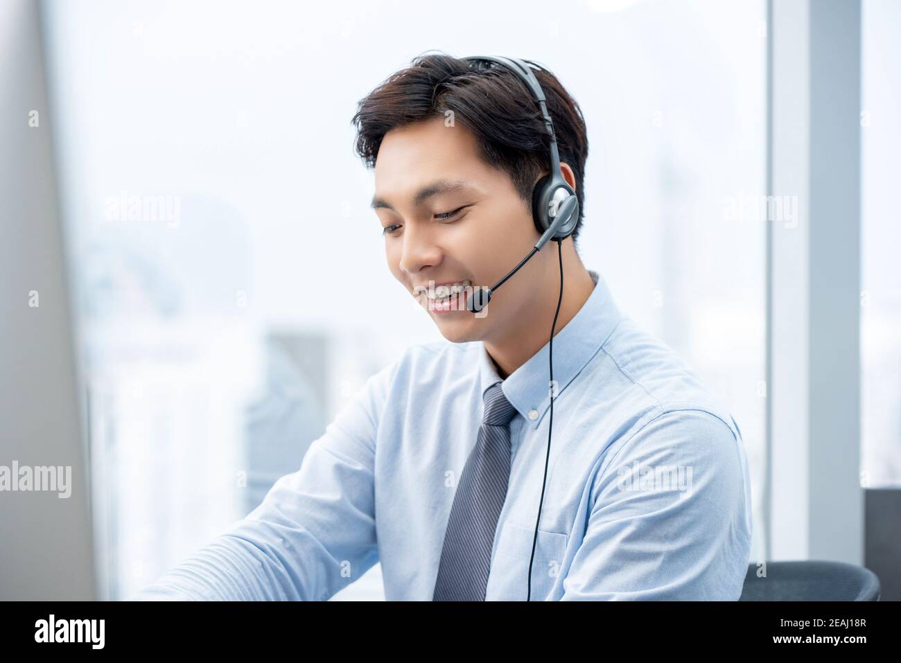Smiling handsome Asian man working in call center office as a customer service operator Stock Photo