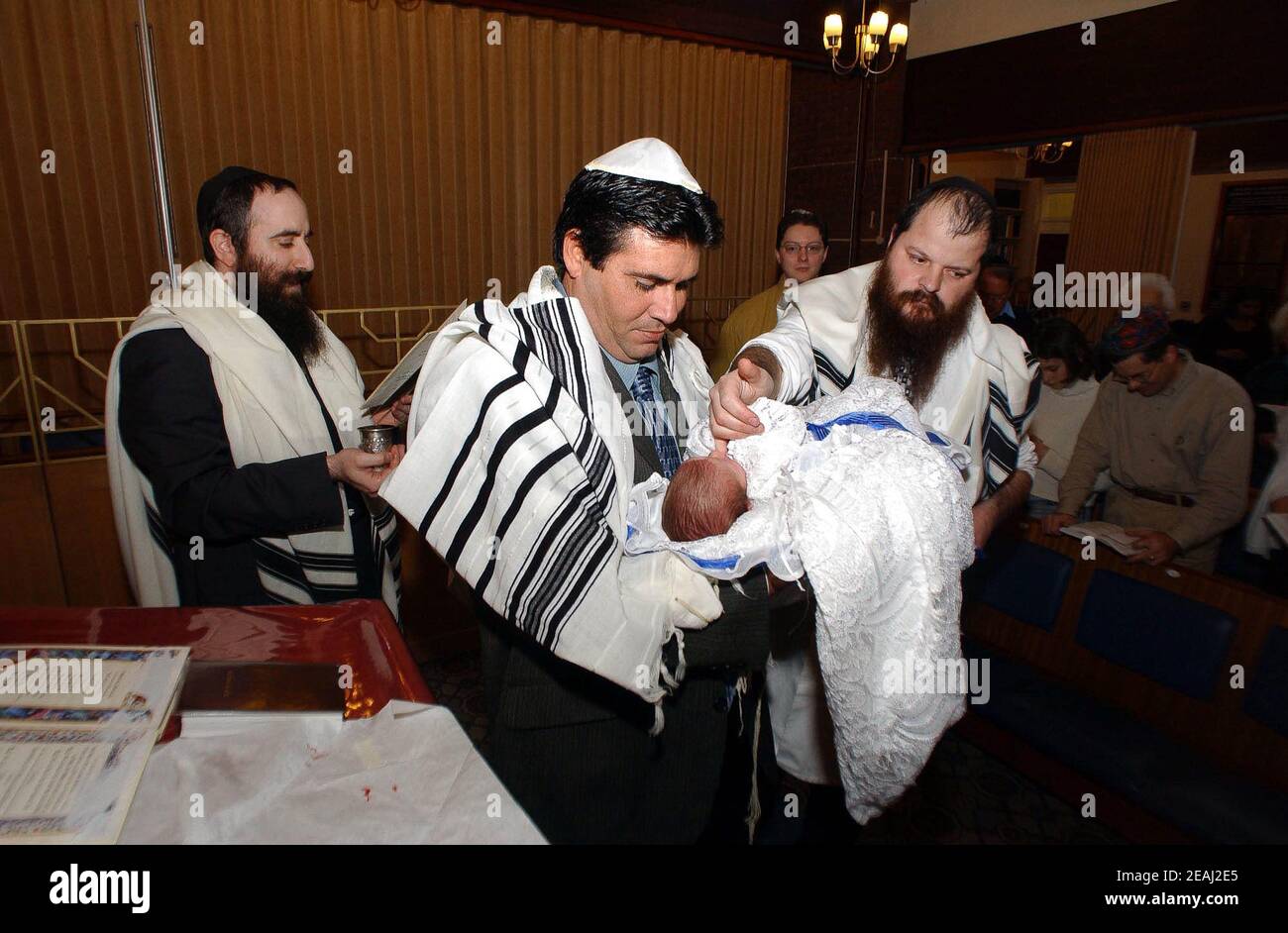 A Brit Milah ceremony takes place on the bimah of the synagogue in the Solihull, West Midlands, as the Mohel gives the traditional blessings as he commences the circumcision watched by the rabbi and family members. Stock Photo