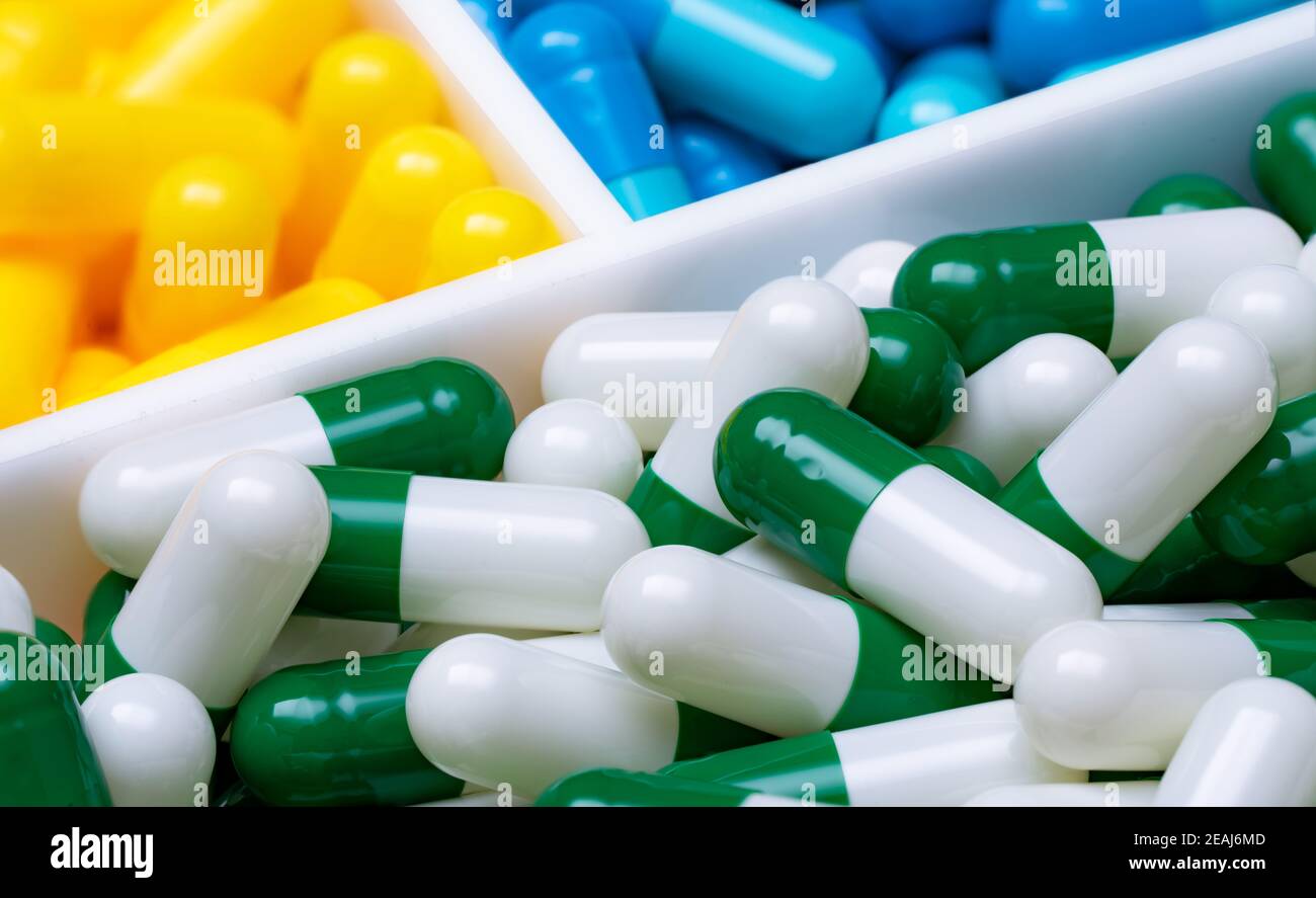 Selective focus on greenwhite capsule pills in plastic box on blurred blue and yellow capsule