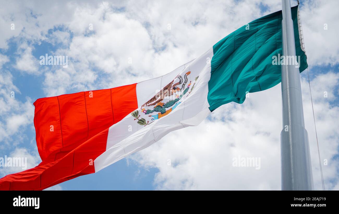 Mexican Flag Waving in the Wind and a Slightly Cloudy Blue Sky as the Background Stock Photo