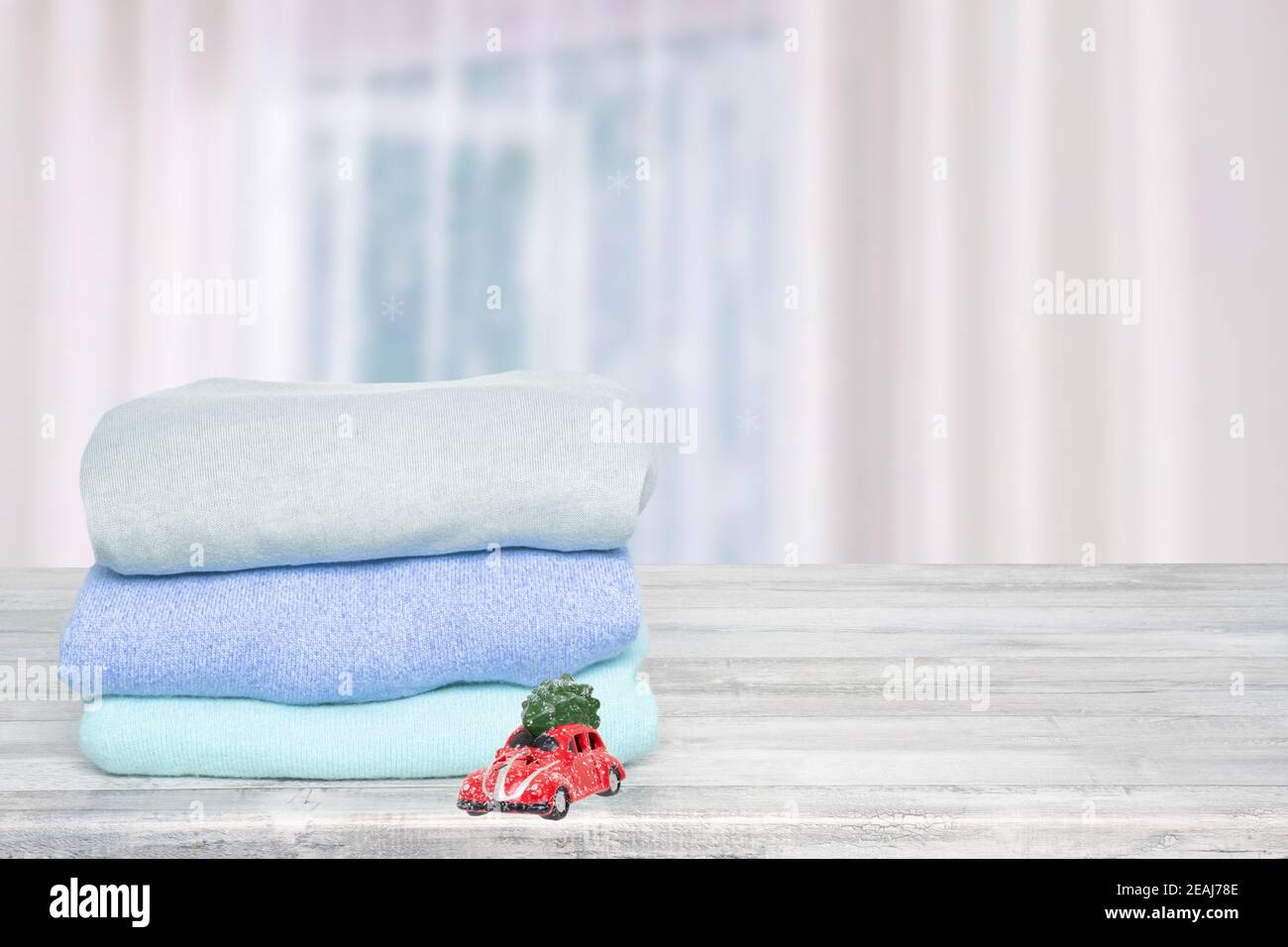 Template for christmas sale. Pile of colorful knitted cozy warm cashmere sweaters  on a wooden table against abstract blurred bright curtain background. Autumn and spring clothing with space for display product montage. Stock Photo