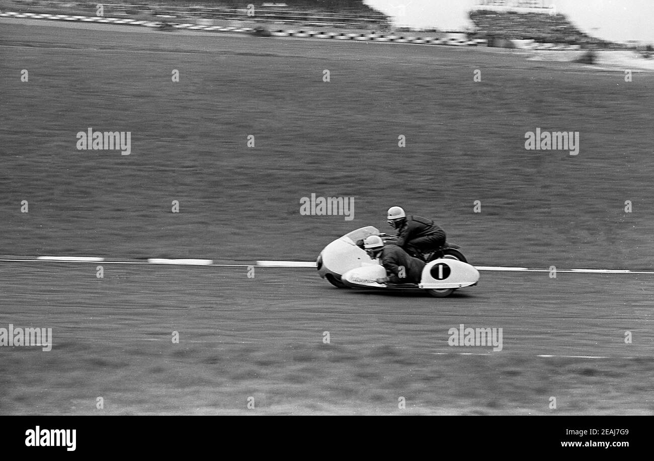 1960s, historical, motor sport, sidecar racing, a motorbike rider and sidecar passenger on their vehicle - numbered one - on the race track, England, UK. Sidecar racing is a sport using a custom-made 3-wheeled motorcycle and is the only form of motorsport where the passenger and driver both steer the vehicle. The vehicle travels at high speeds and the sport is exciting to watch. Both rider and passenger are wearing the traditional black leather outfits of the era. Stock Photo