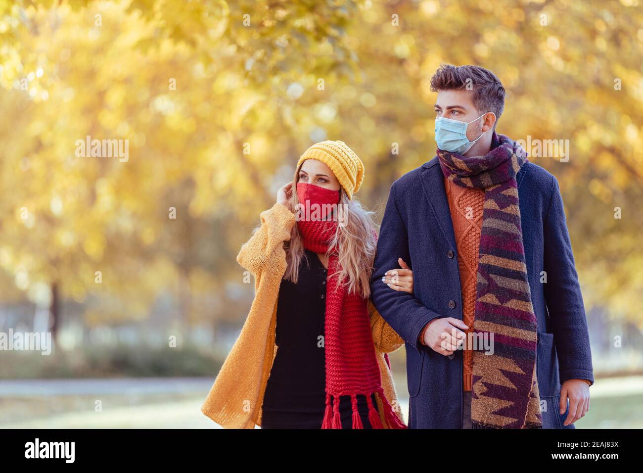 Couple wearing mask walking in autumn park Stock Photo