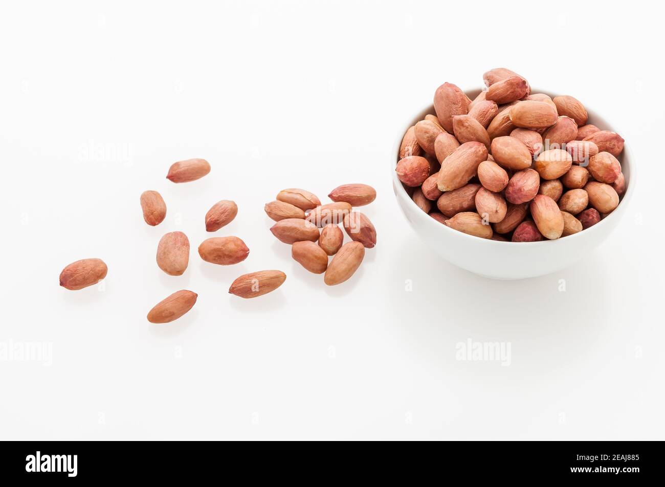 Peeled peanuts in a white ceramic cup and scattered grains on a Stock Photo