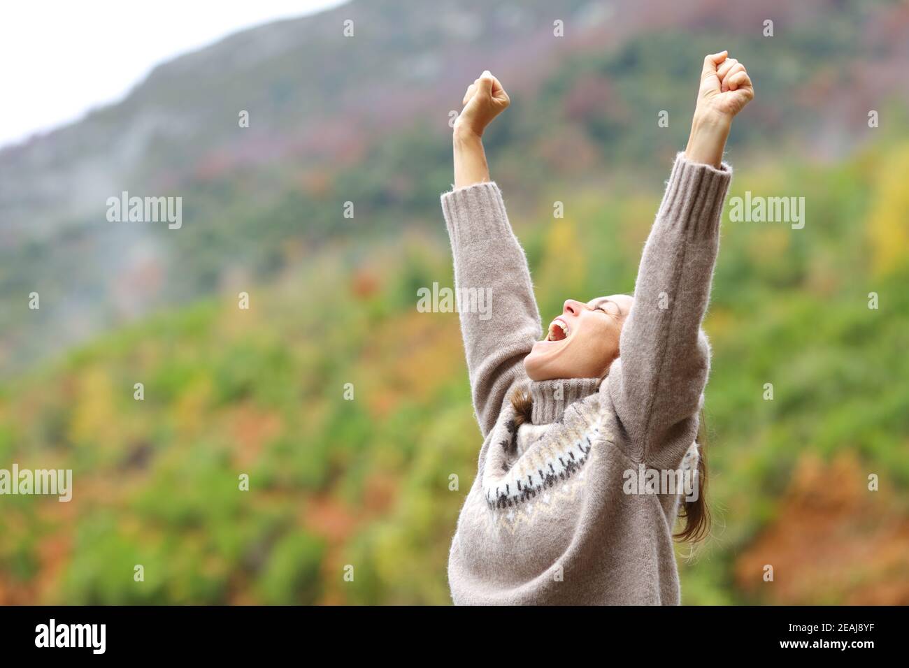 Middle age excited woman raising arms in the mountain Stock Photo