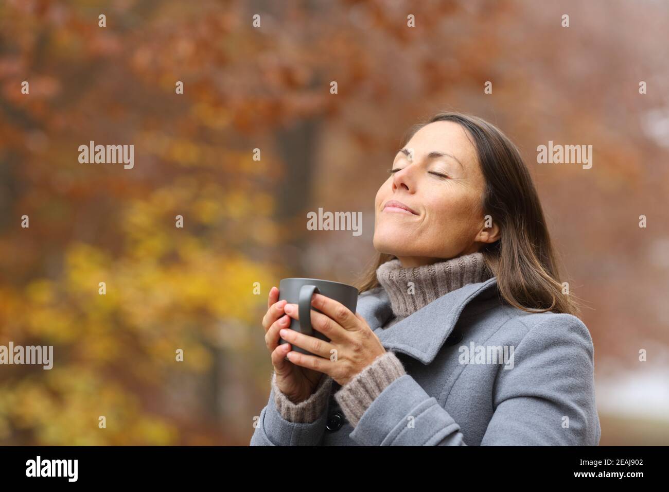 Relaxed middle age woman with coffee breathing in fall Stock Photo