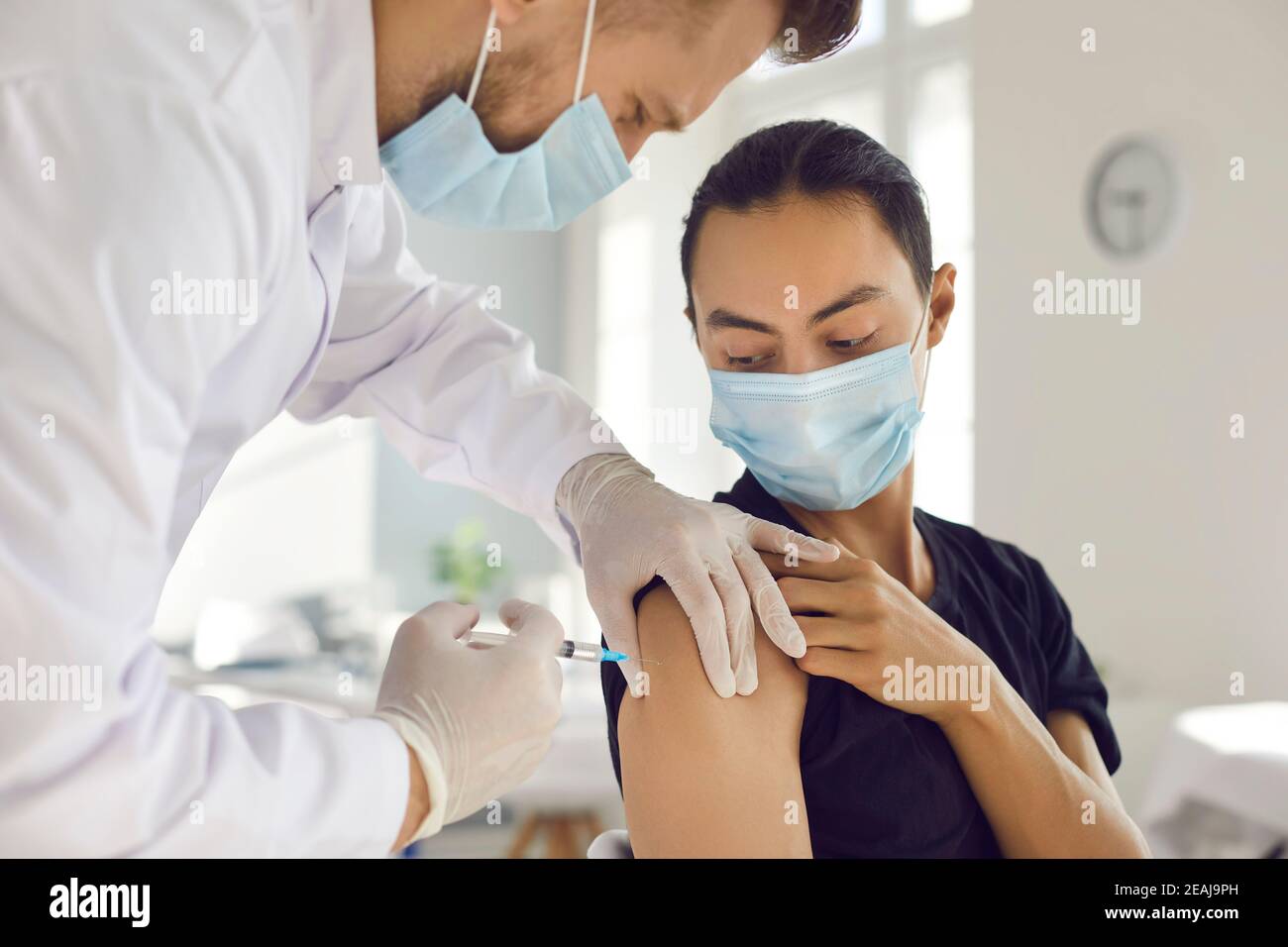 Asian man patient in protective mask looking at doctor man medical worker making vaccination injection Stock Photo