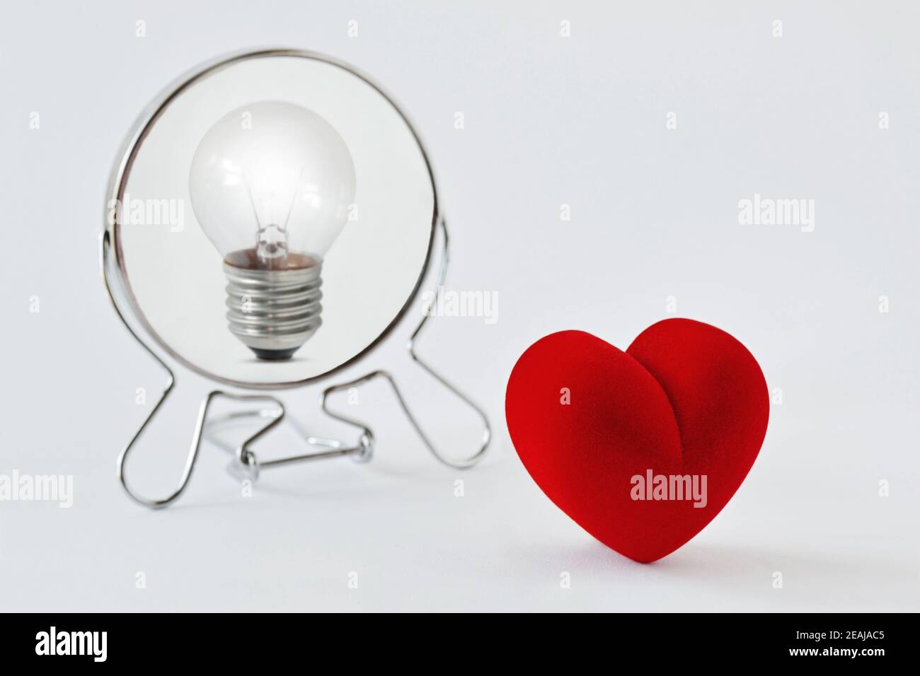 Heart looking in the mirror and seeing itself as a light bulb - Concept of dualism heart/mind, emotion/reason Stock Photo