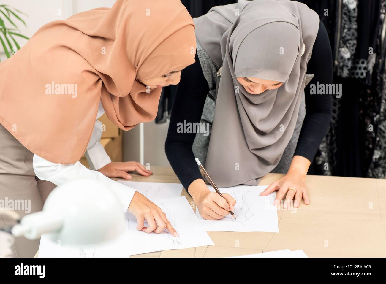 Muslim woman fashion designer drawing dress sketches working together with her colleague in tailor shop Stock Photo