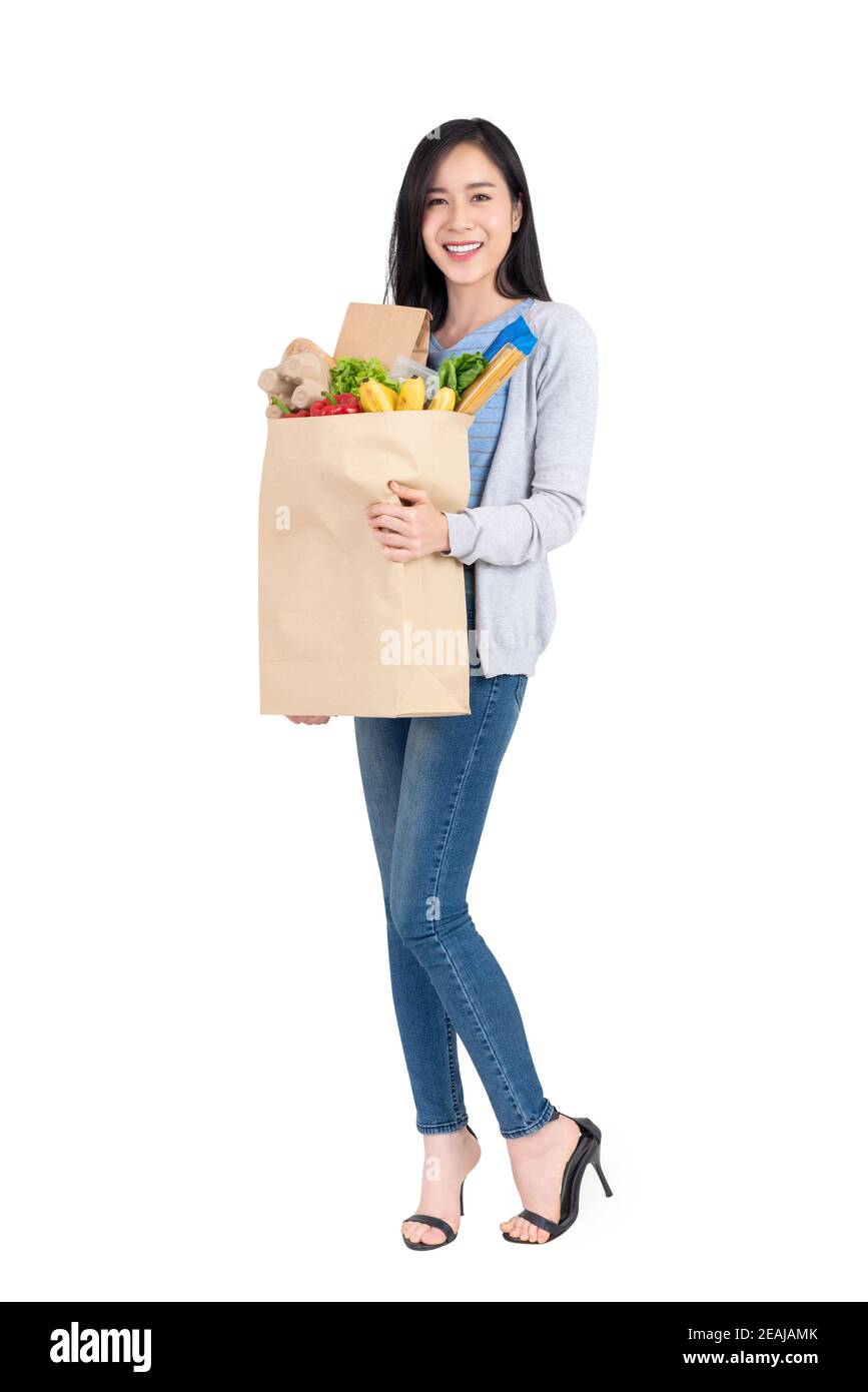 Beautiful smiling Asian woman holding paper shopping bag full of vegetables and groceries studio shot isolated on white background Stock Photo