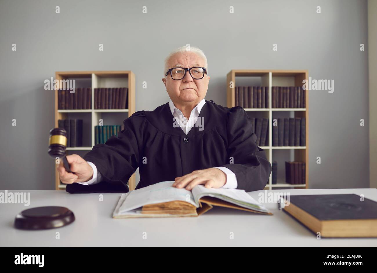 Senior man professional judge sitting in conference hall during trial and striking with hammer Stock Photo