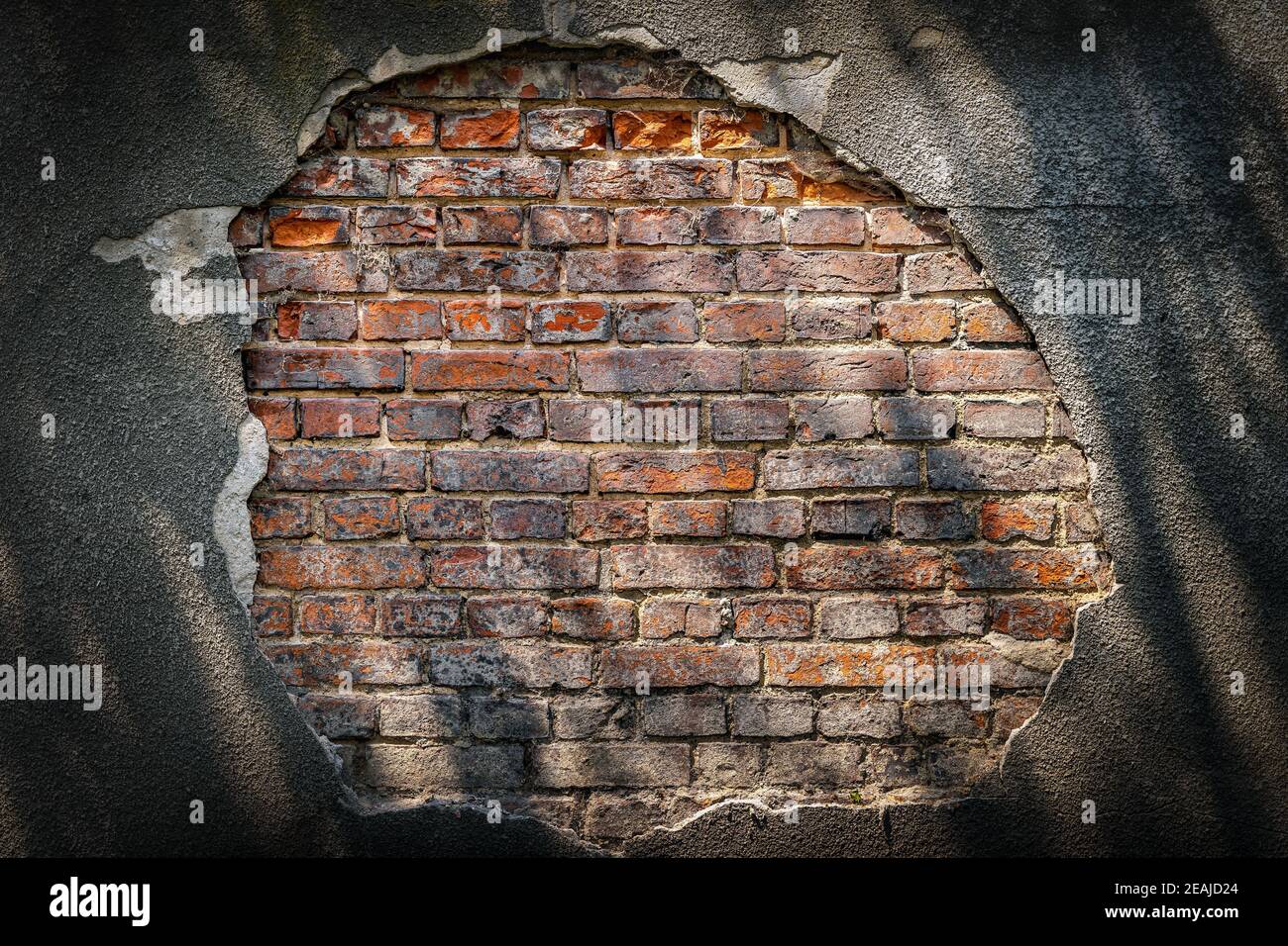 Rustic red corroded brick hole in plaster wall with light and shadow patterns Stock Photo