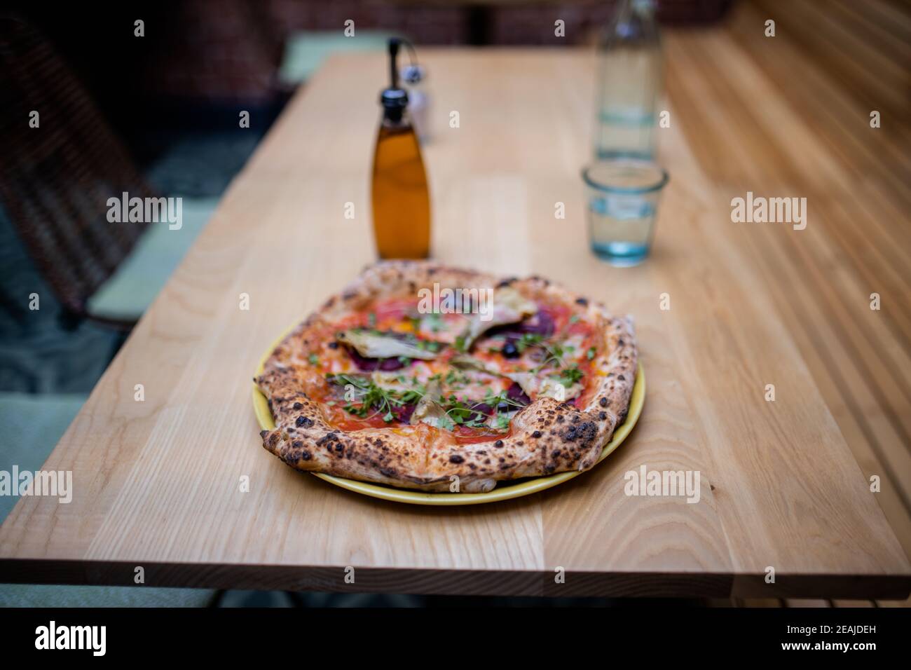 Vegan pizza on a table alongside a bottle of dressing and a glass of water Stock Photo