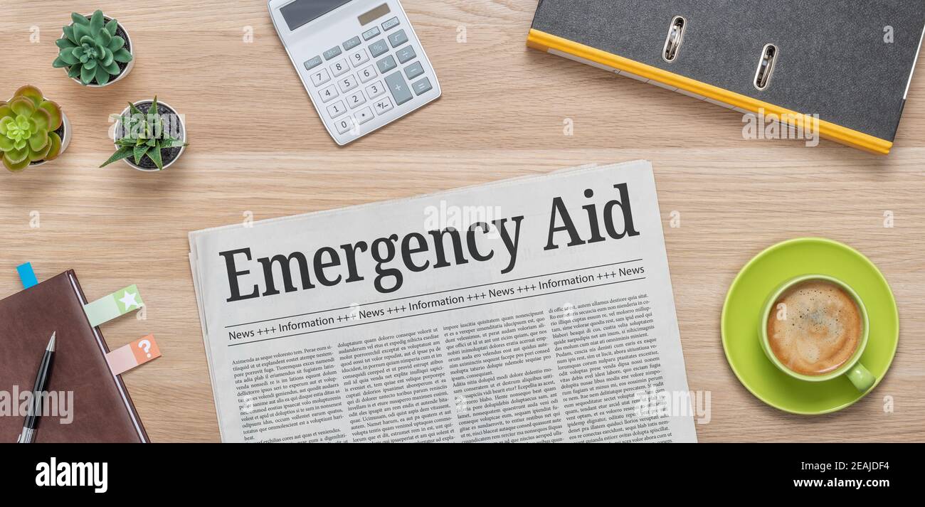 A newspaper on a desk with the headline Emergency Aid Stock Photo