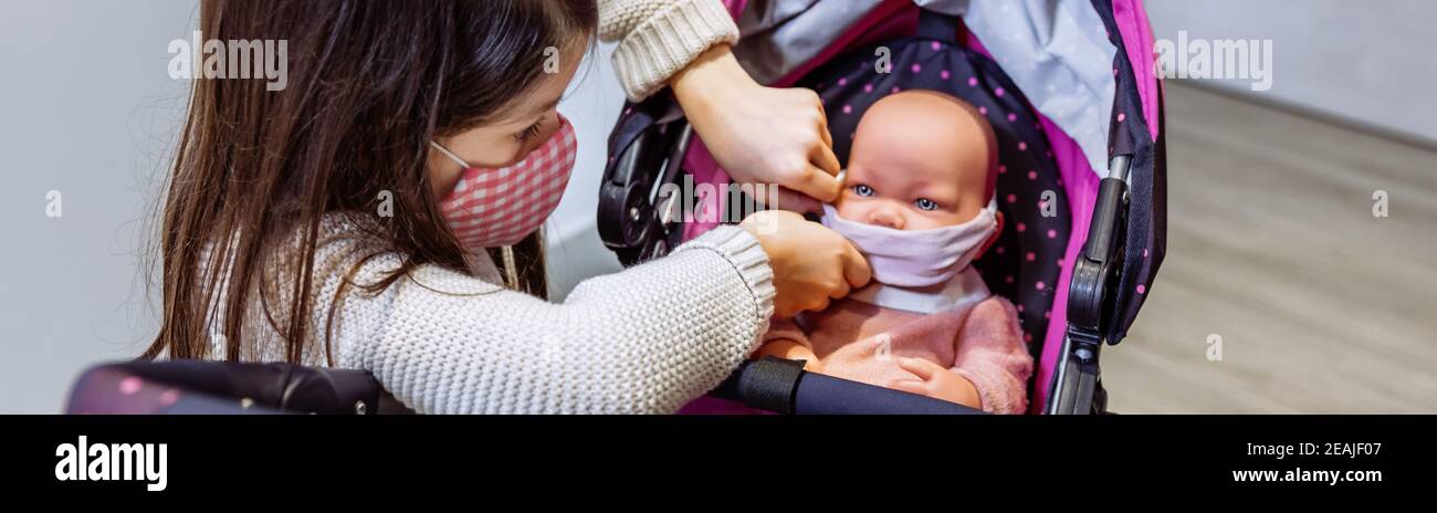 Girl with face mask putting mask on her baby doll Stock Photo