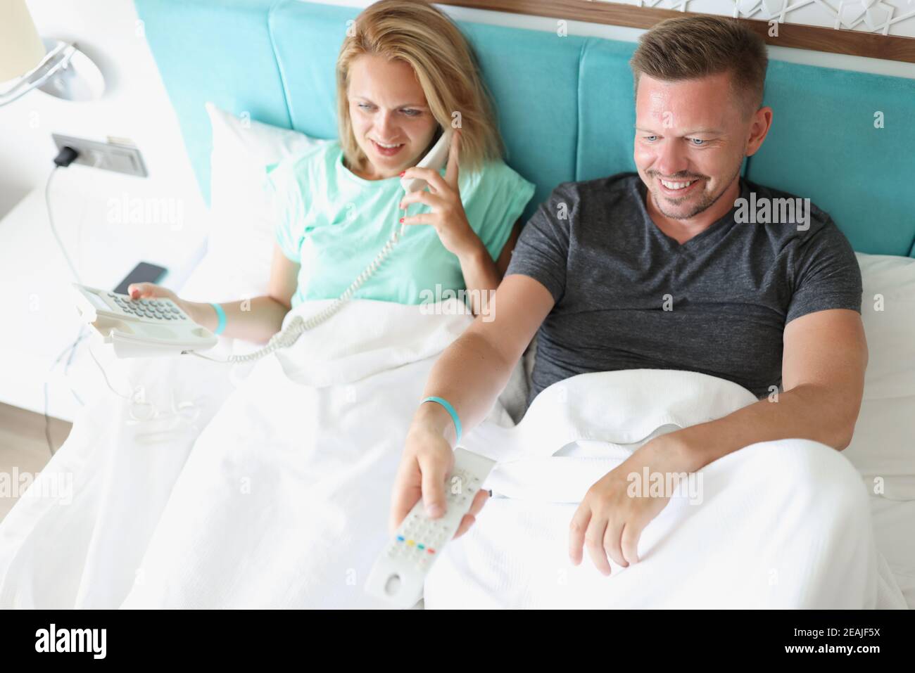 Man and woman are lying on bed. Woman is talking on phone, man switches ...