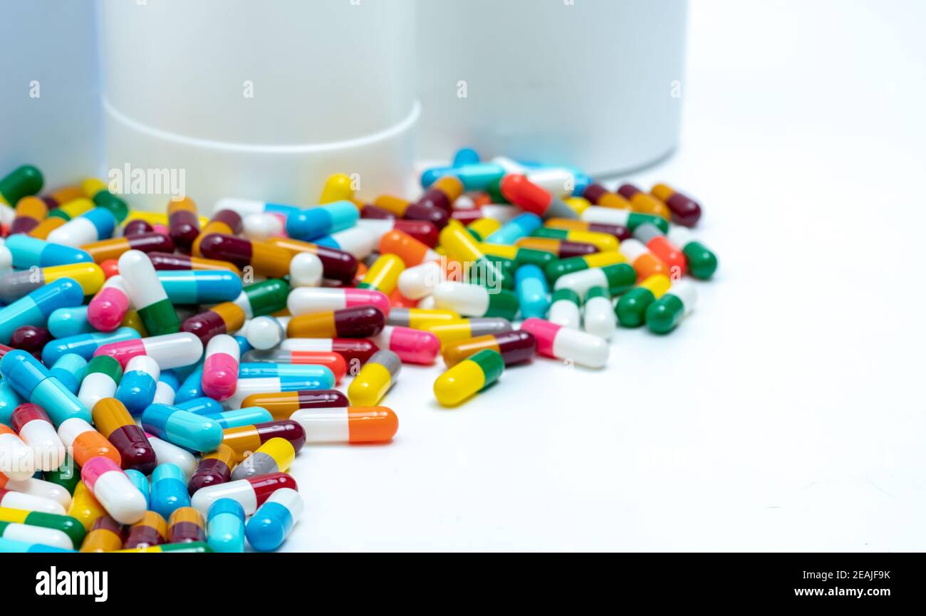 Colorful capsule pills near plastic drug bottle. Multicolored capsule pills on white table