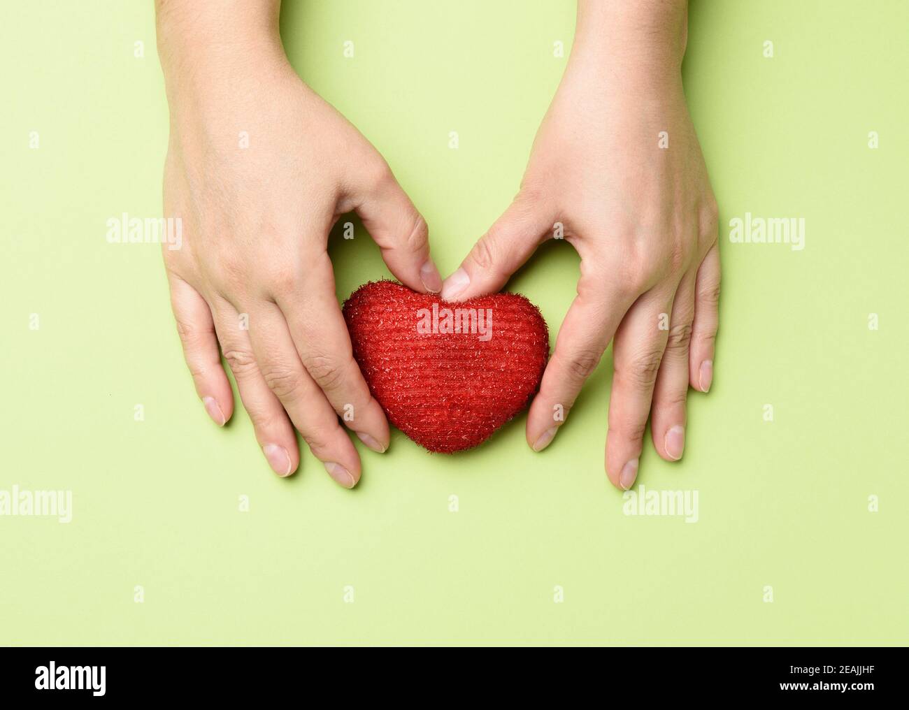female hands holds red textile heart, green background Stock Photo