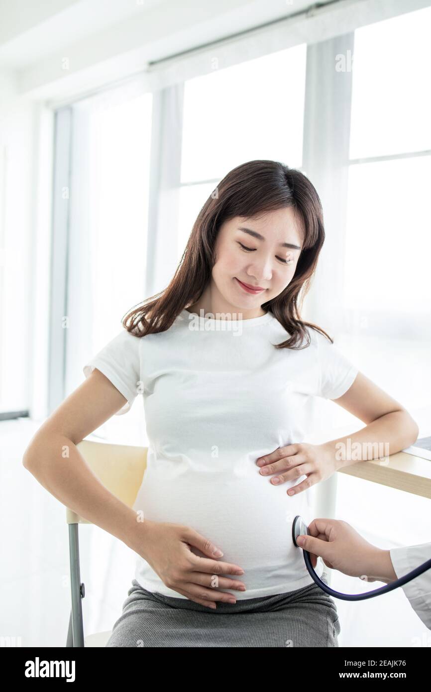 Female Obstetrician doctor with stethoscope listening to pregnant woman