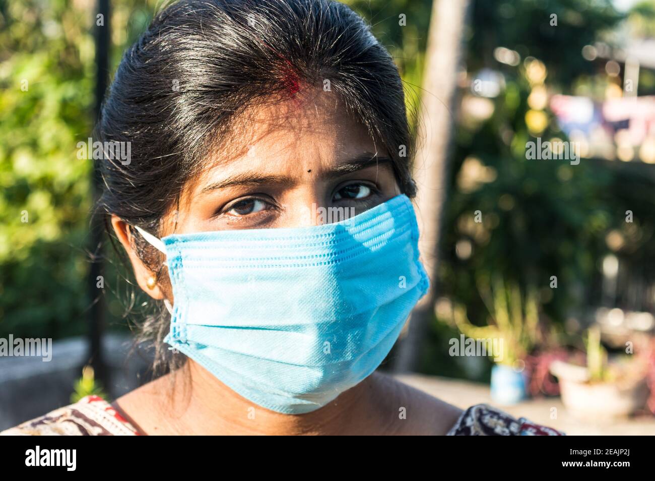 Smiling face wearing mask. Woman smiling wearing a face mask. Close up Front view of a happy Indian woman wearing a face mask smiling and looking at camera. Healthcare medicine background India. Stock Photo