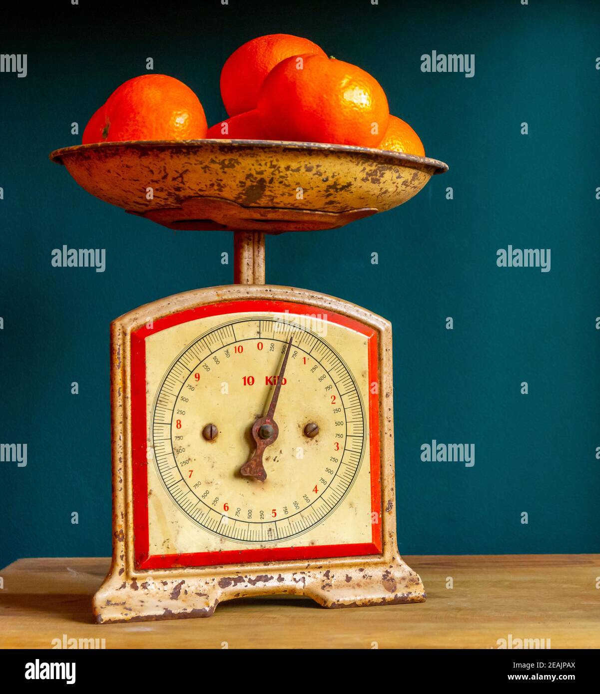 Weighing tangerines in a retro, vintage and worn out scale or balance, on a wooden plank against a guatemala green wall. Stock Photo