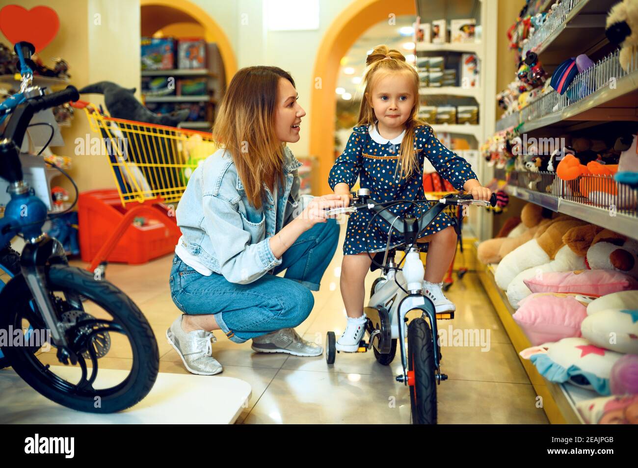 Mom and little girl choosing bicycle, kid's store Stock Photo