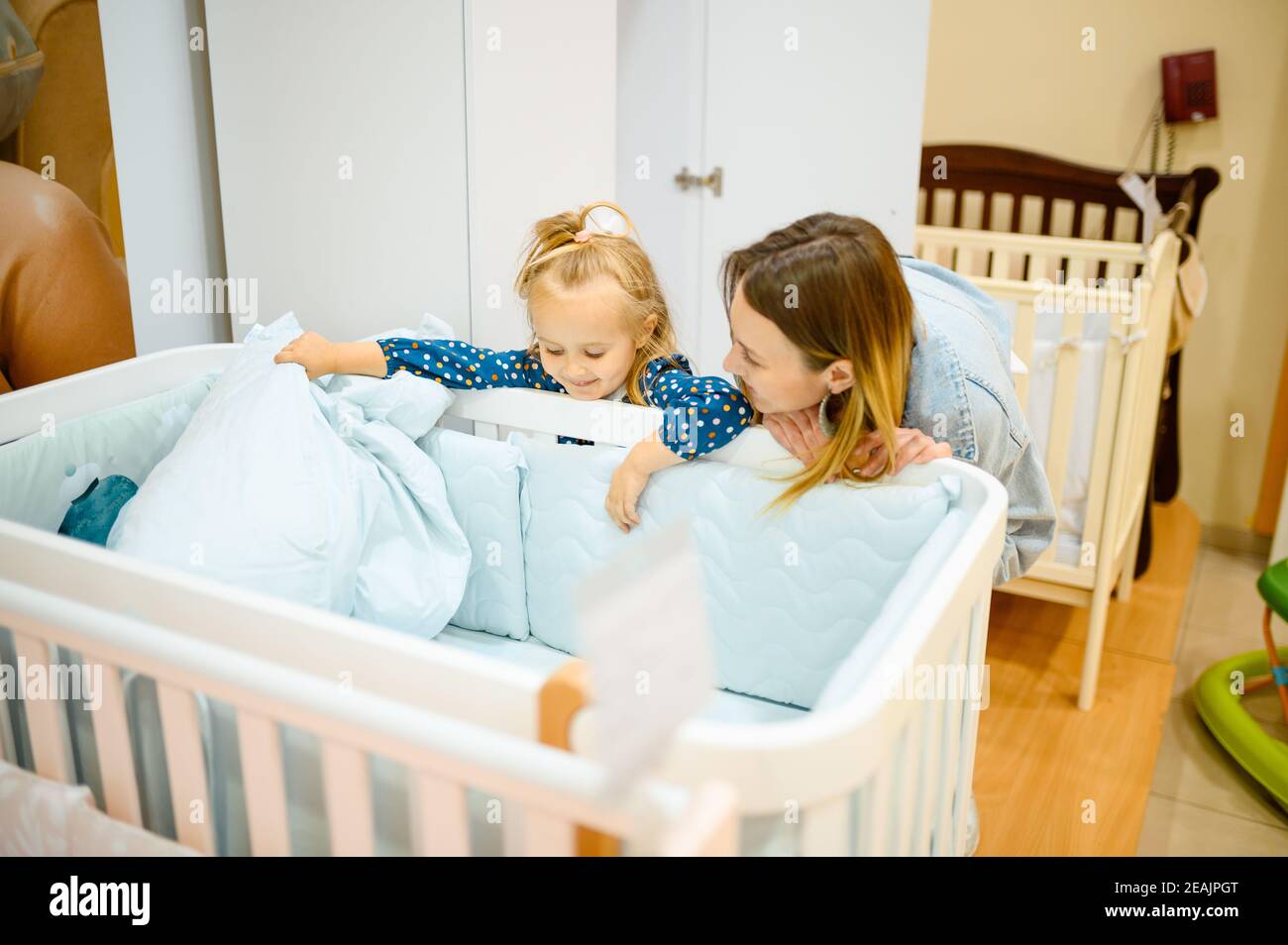 Mother and little daughter buying baby bed Stock Photo Alamy