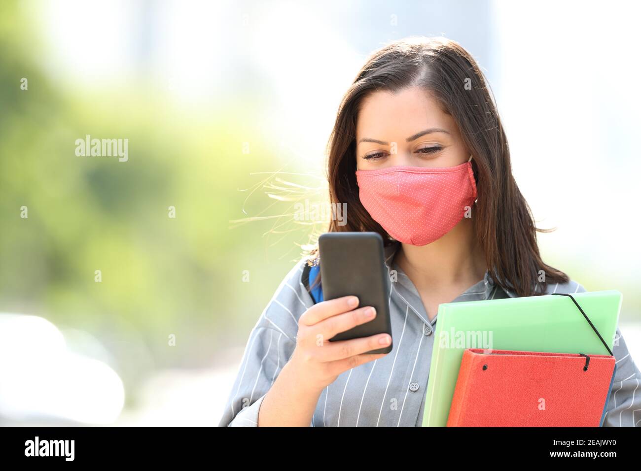 Student with mask using smart phone in the street Stock Photo
