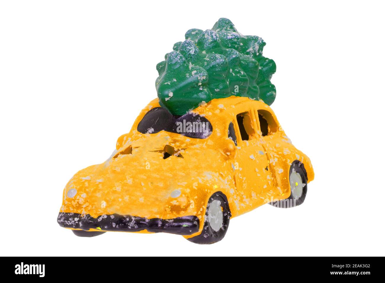 Christmas decorations background. Closeup of a snow-covered yellow car toy with green fir-tree on the roof isolated on a white background. Saisonal design element for cards or stickers. Macro. Stock Photo