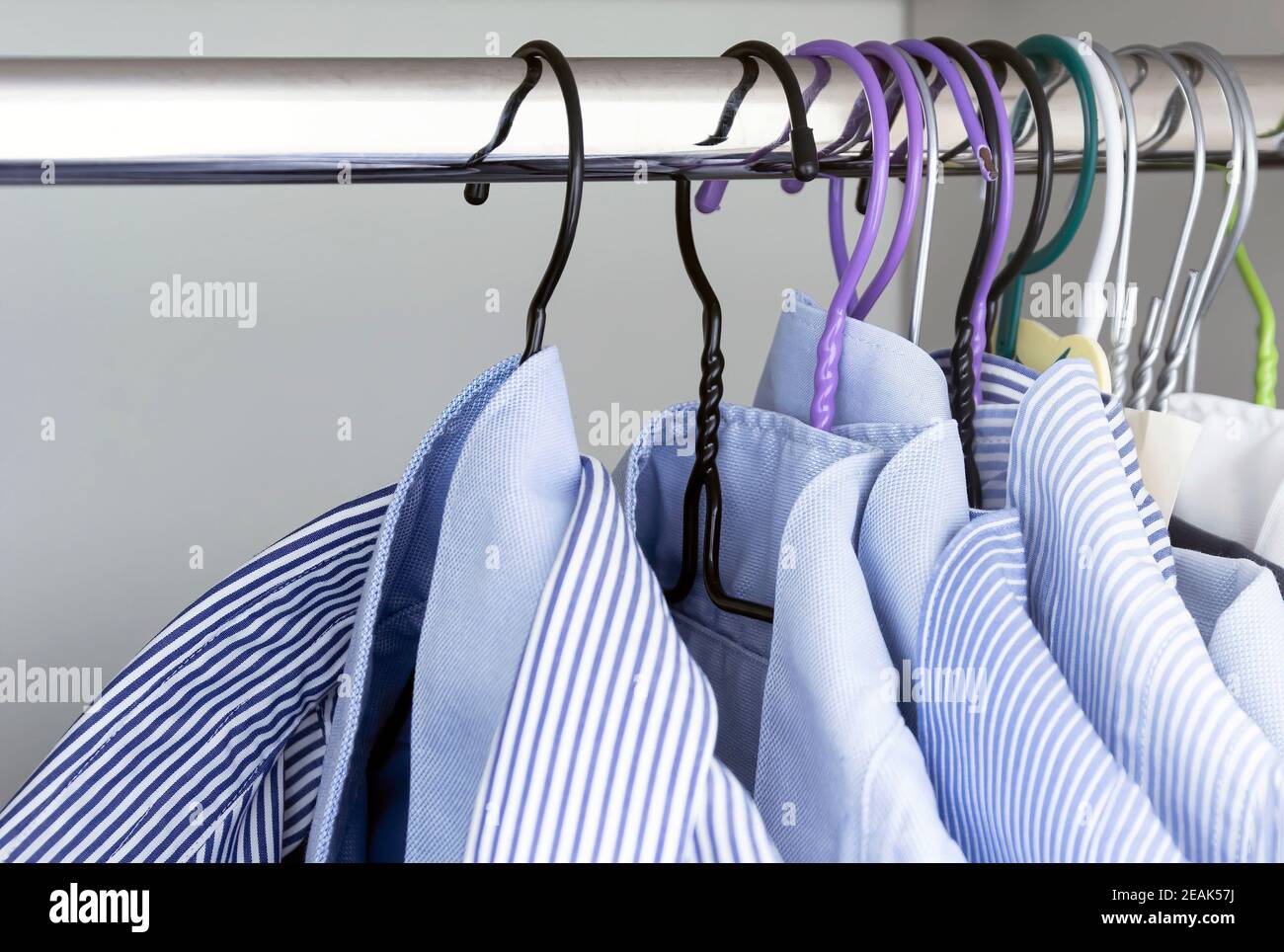 Group of light blue striped shirts hanging on the rod of a white