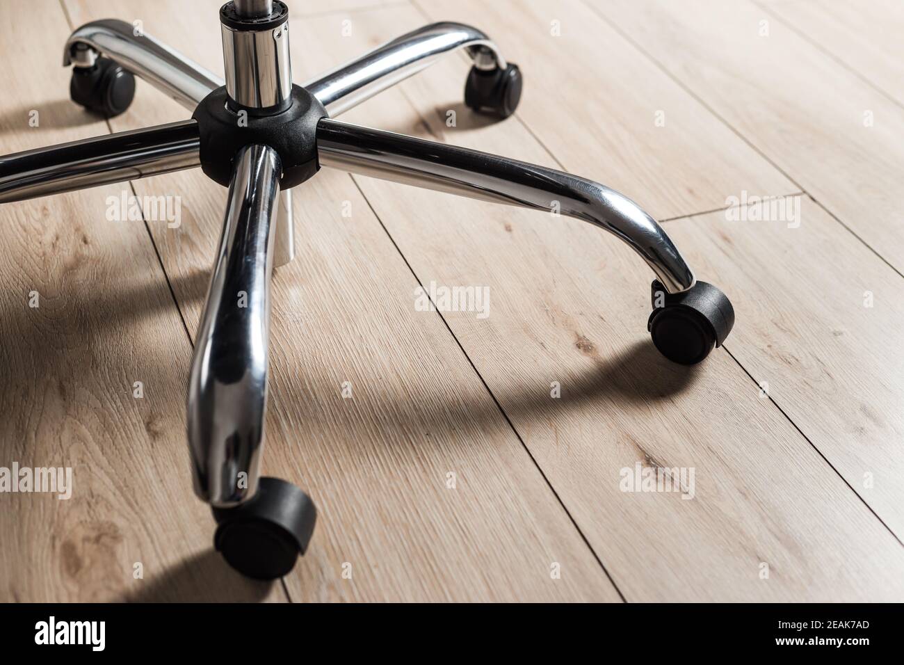Metal base of office chair with wheels on wooden floor, closeup Stock Photo