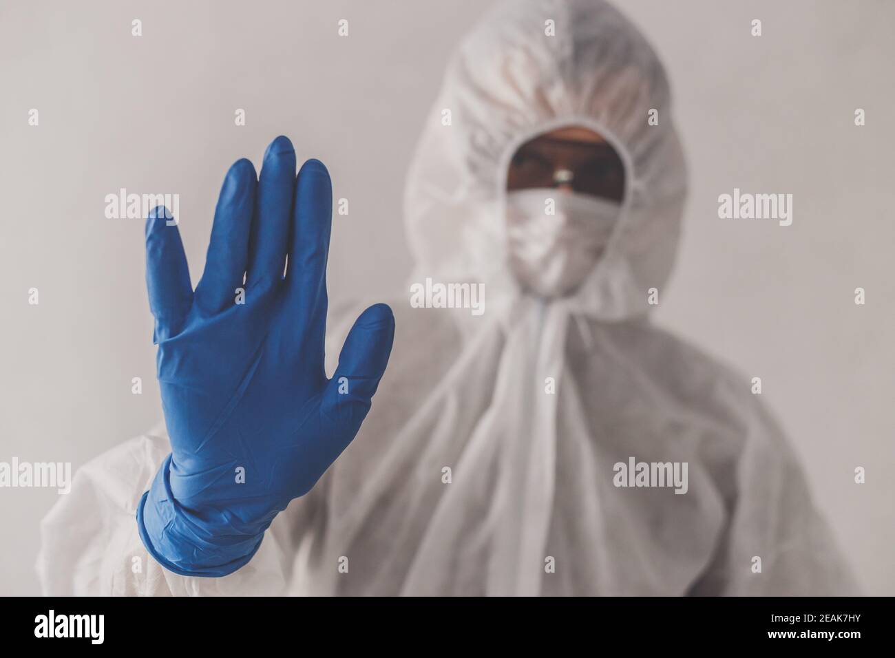 Epidemic. Man in protective suit, mask gestures stop by hand in glove. Stock Photo